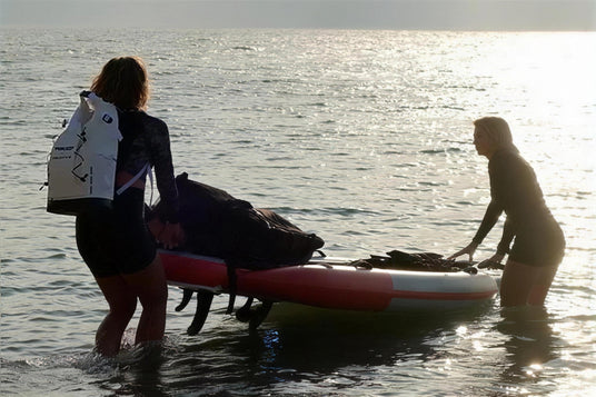 Two riders launching a loaded Waydoo UniRide Explore eSUP into the sea at sunset